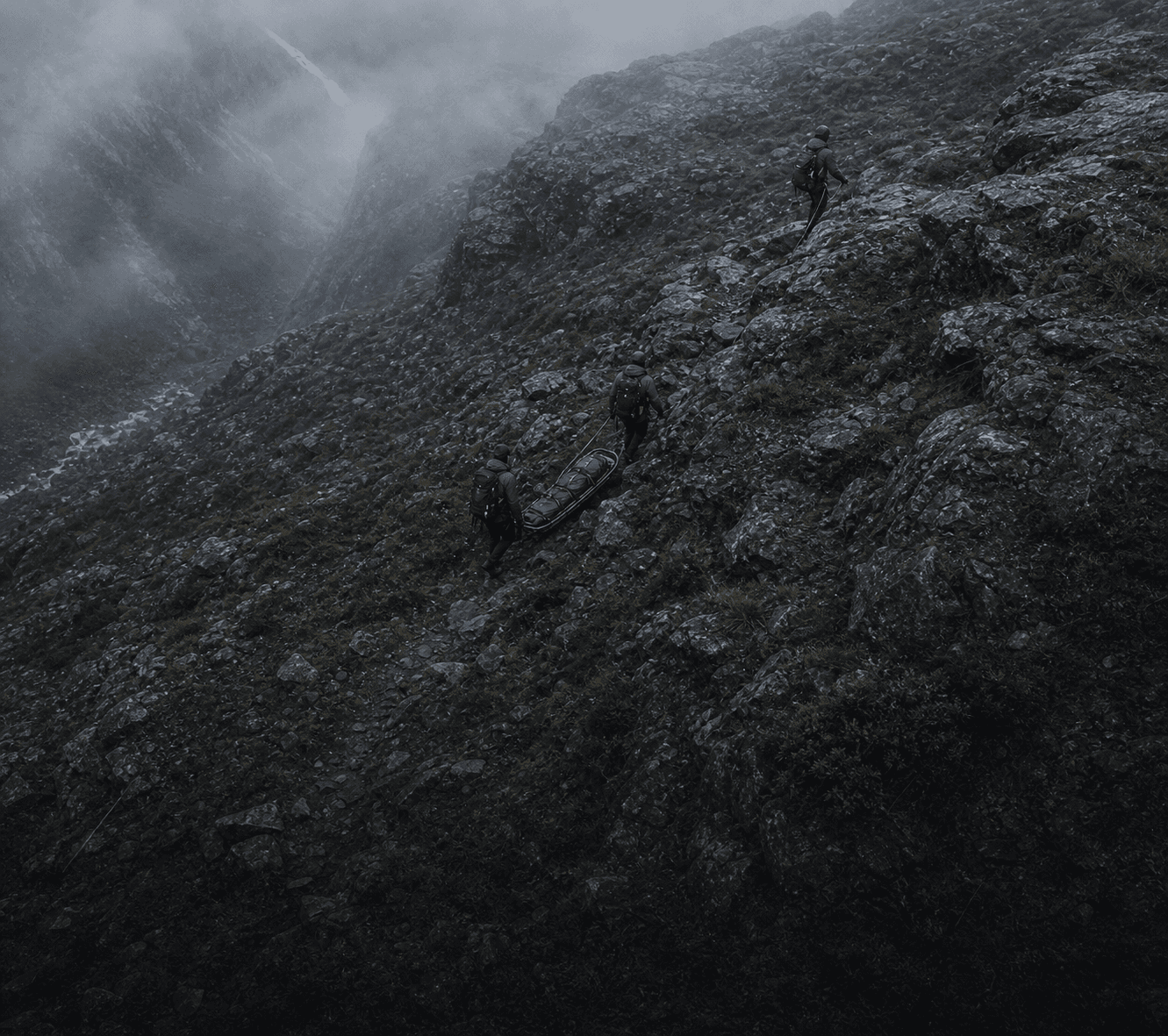 Rescue team carrying a stretcher across a wet mountainside